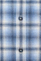 Close-up of a blue and white plaid shirt fabric with buttons.